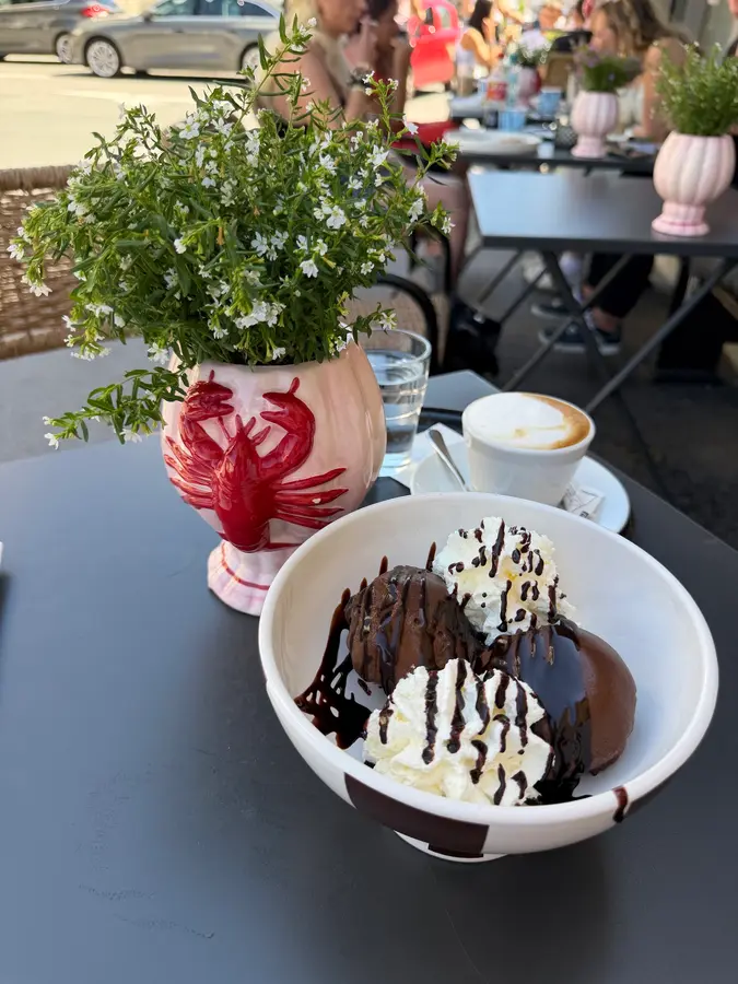 Profiteroles mit Schlagobers und Schokolade, daneben eine rosa Hummer-Vase und ein Cappuccino