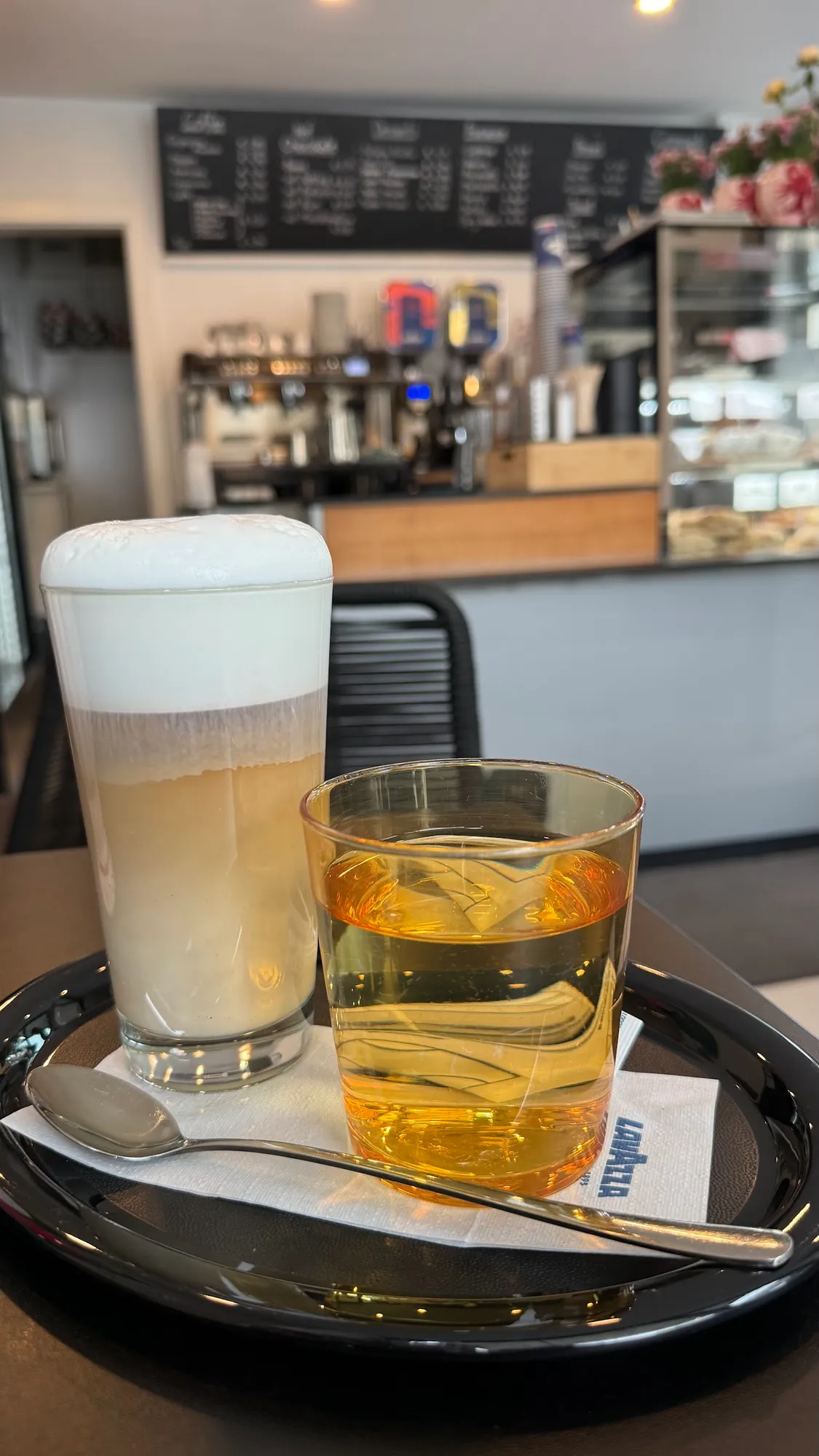 Latte macchiato im hohen Glas und ein Saft auf dem Tablett, dahinter Theke und Kreidetafel