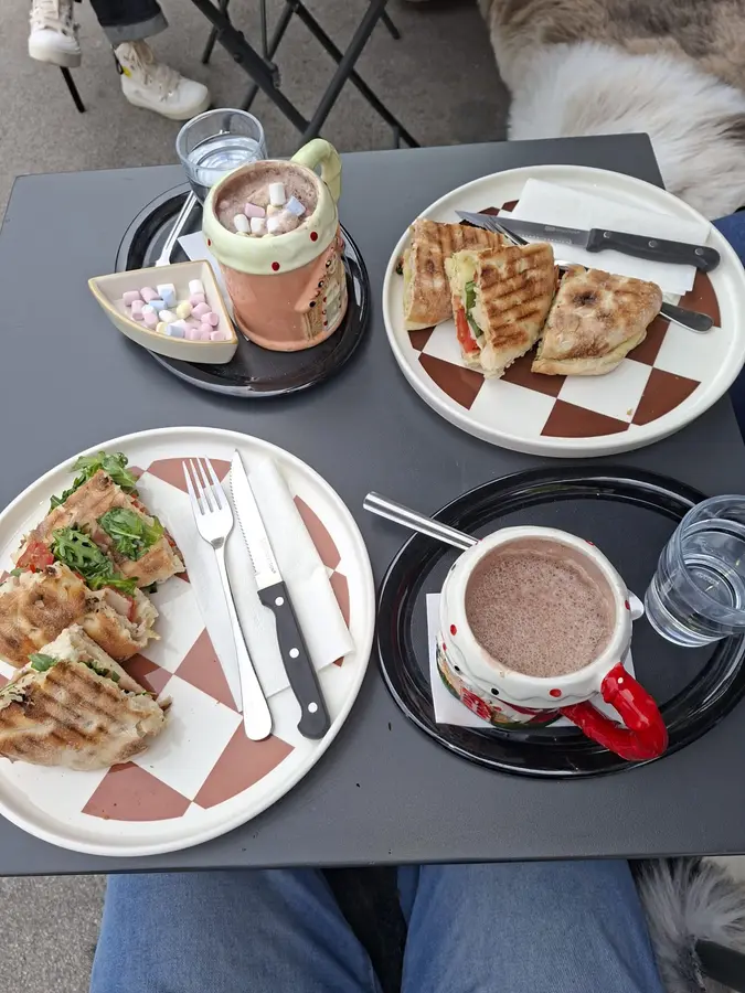 Von oben: zwei Teller mit Focaccia-Sandwiches und zwei Tassen heiße Schokolade, eine mit Marshmallows