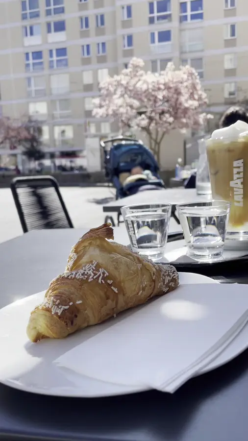Croissant mit Hagelzucker auf dem Tisch draußen, dahinter eine blühende Magnolie